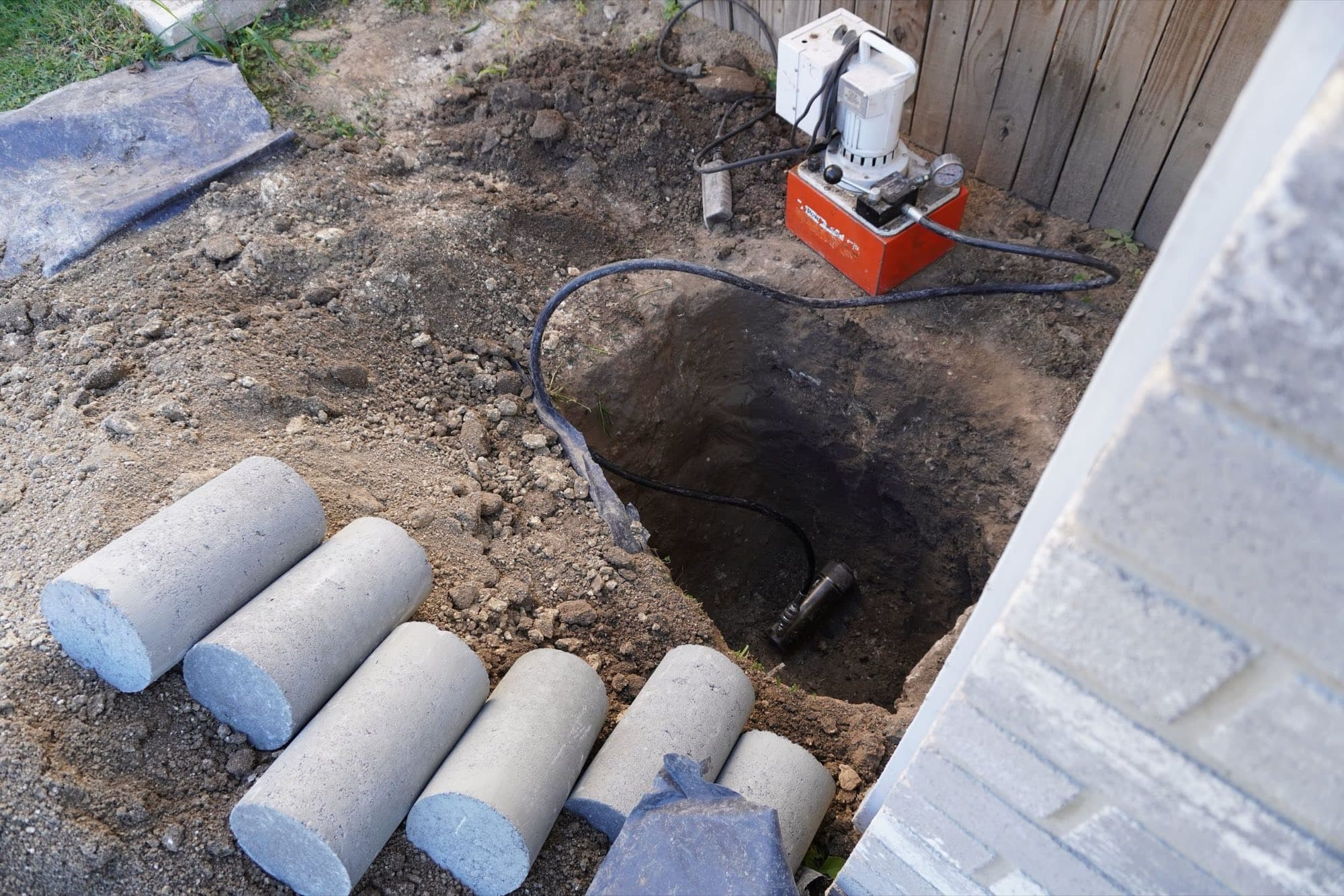 Concrete pier cylinders staged beside an excavated hole with a hydraulic pump