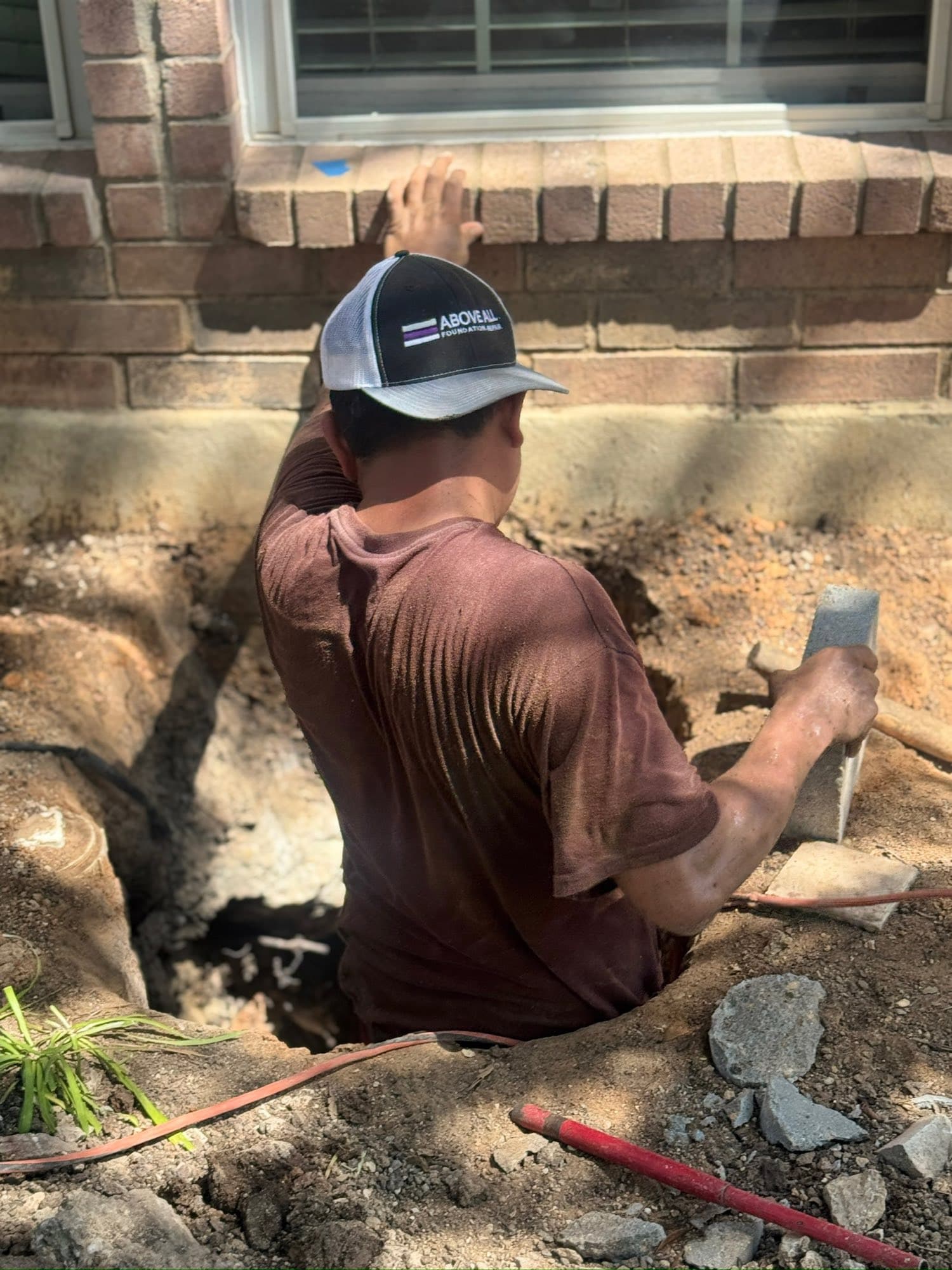 An Above All crew member working in an excavated pier hole beneath a brick home