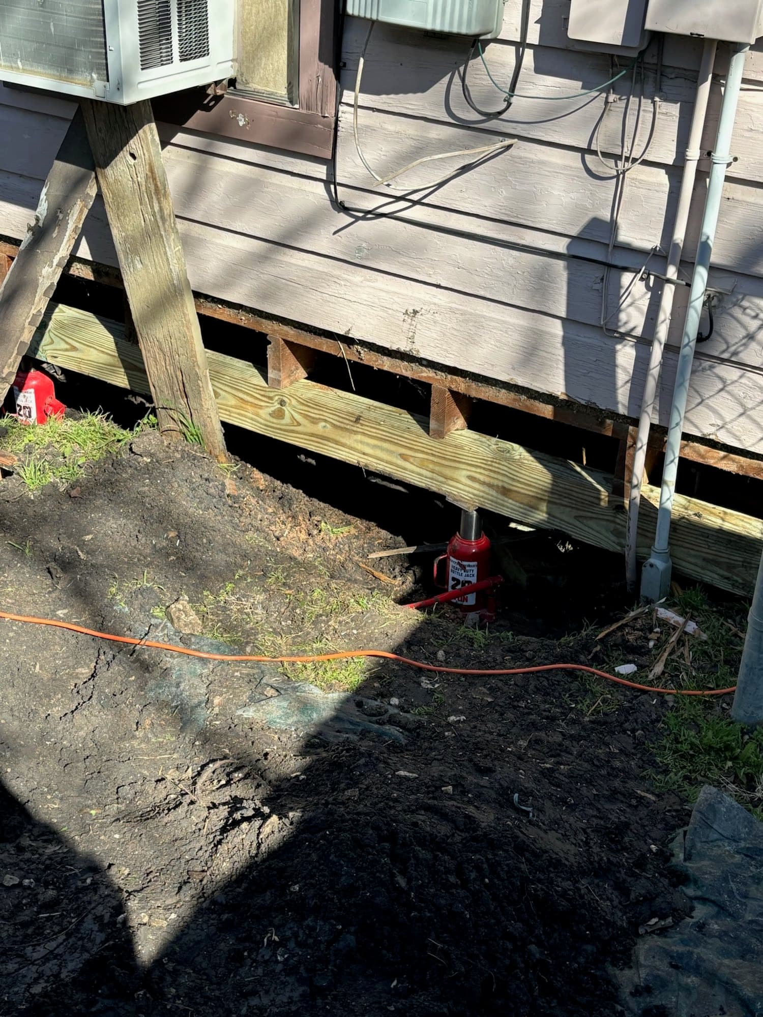 A bottle jack lifting a new treated support beam beneath a pier and beam home
