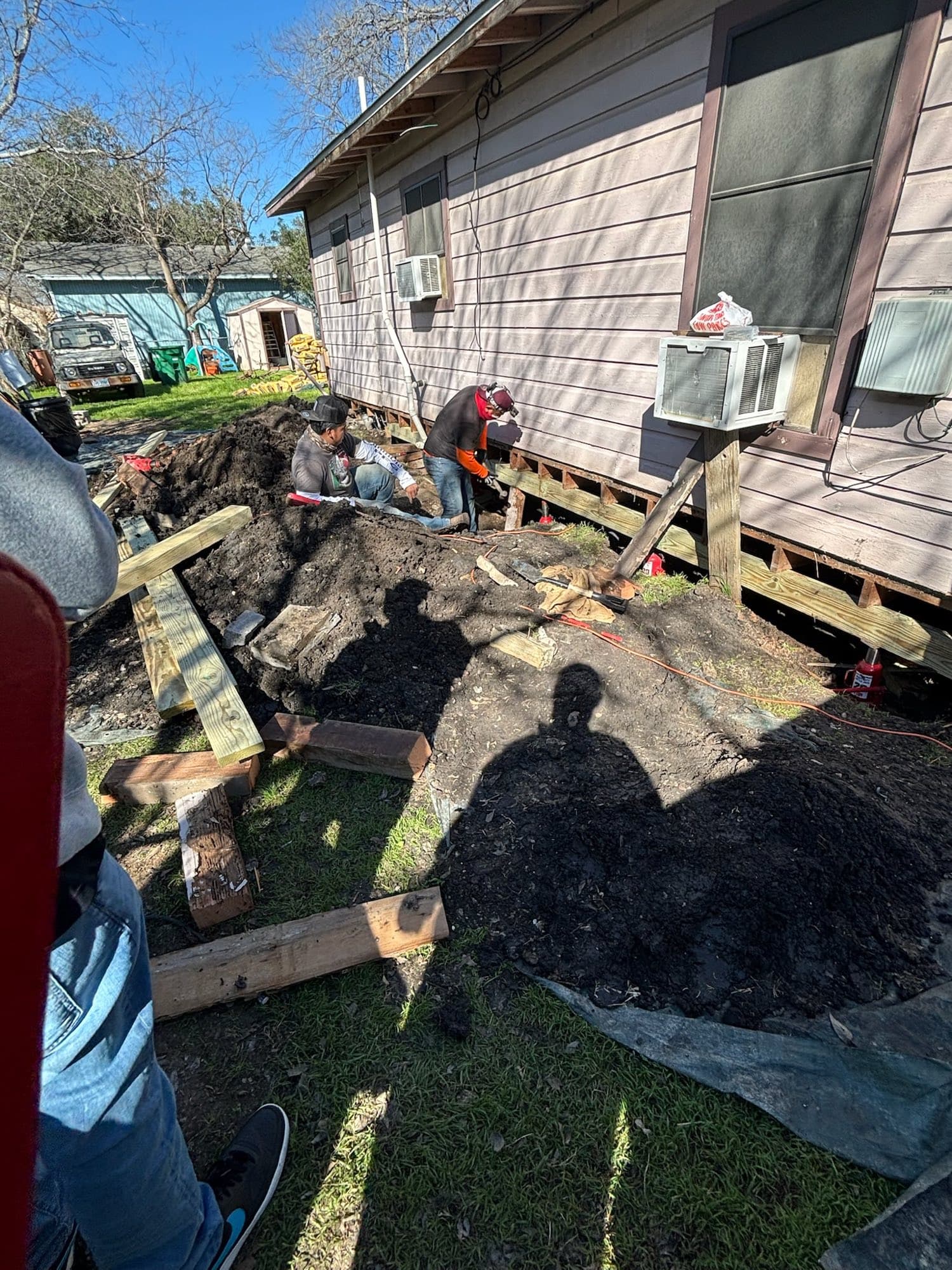 A crew working along the side of a pier and beam home
