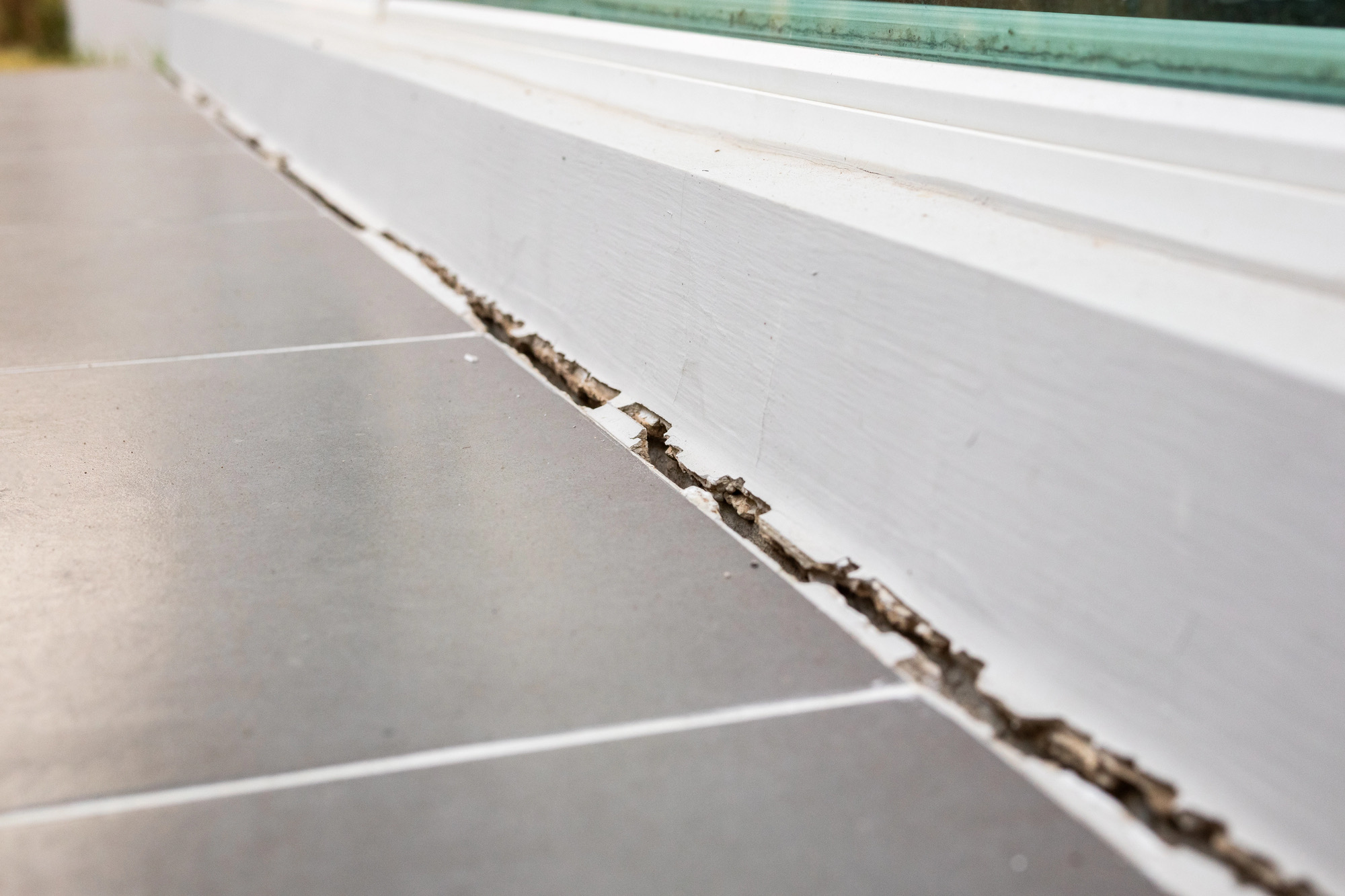 Caulk line split open where a tile floor meets the baseboard under a window